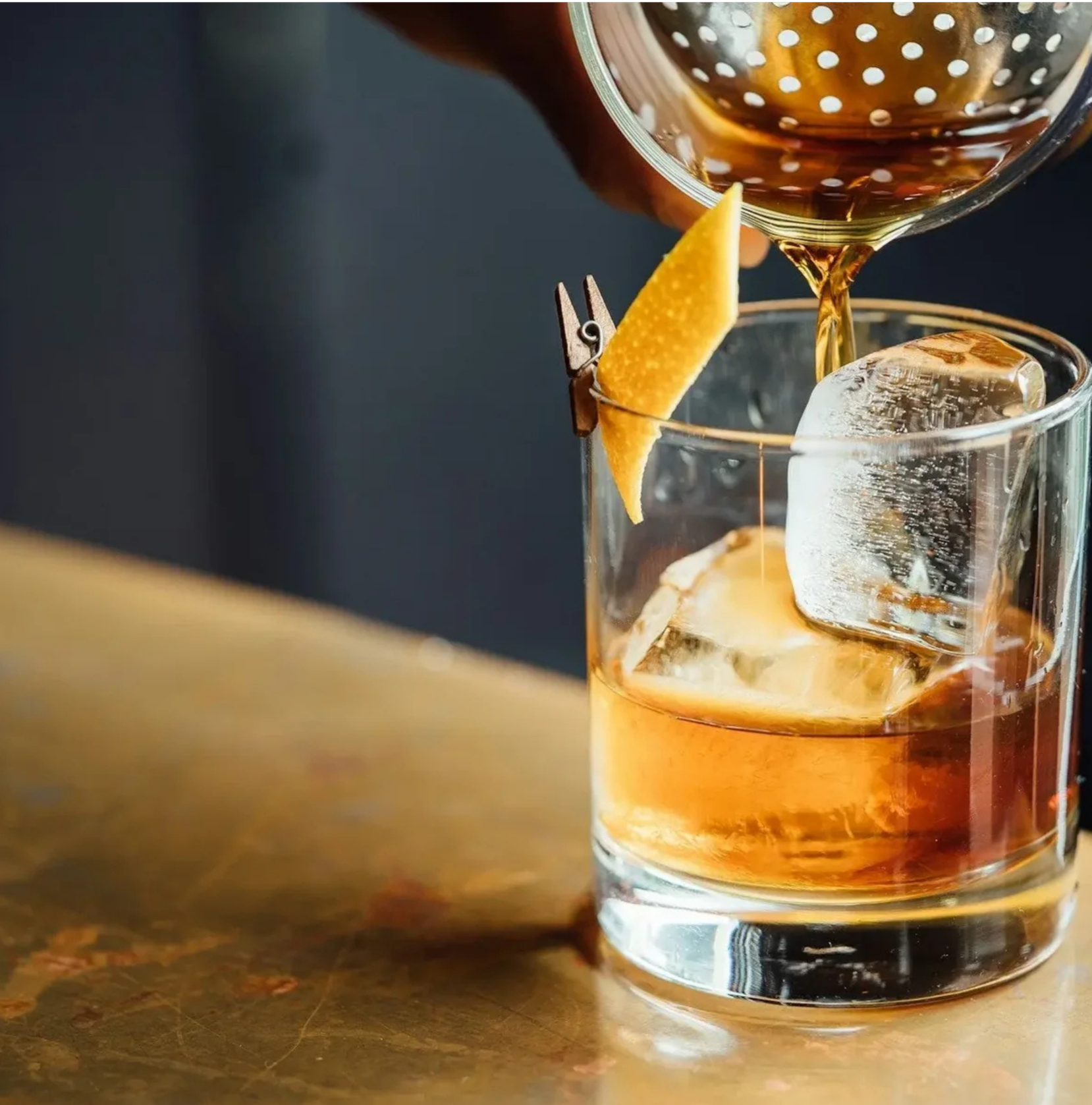 Pouring a dark cola drink into a glass with ice and a lemon wedge garnish.