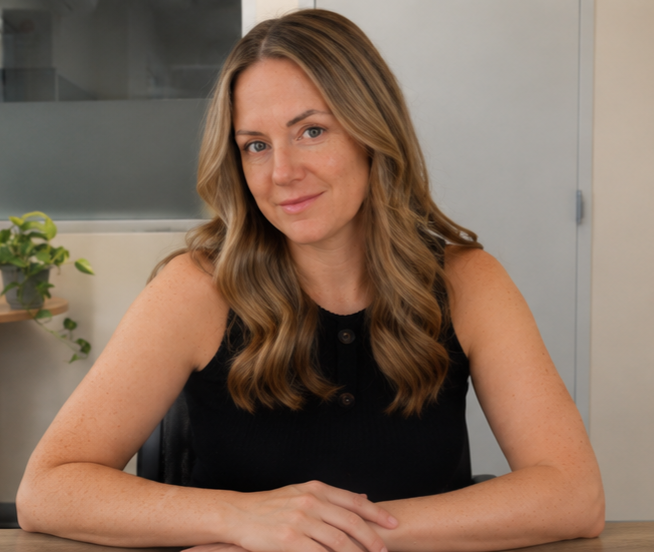 A woman with light brown hair wearing a black sleeveless top sitting at a table.