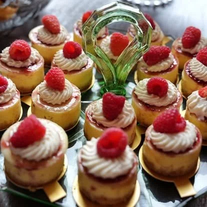 Tray of mini cheesecakes topped with whipped cream and fresh raspberries