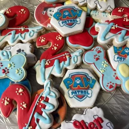 Paw Patrol themed decorated cookies in red, blue, and white colors, including bone shapes, number 2, repeated words, and character logos.
