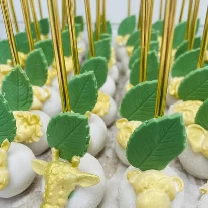Cake pops decorated with green leaves and yellow flowers, each with a gold stick.