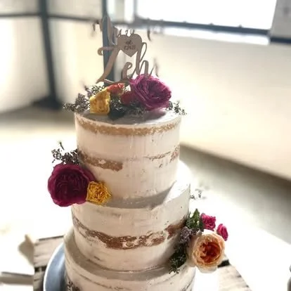 A three-tiered naked wedding cake decorated with large pink, yellow, and orange flowers and topped with a '10th' anniversary cake topper.