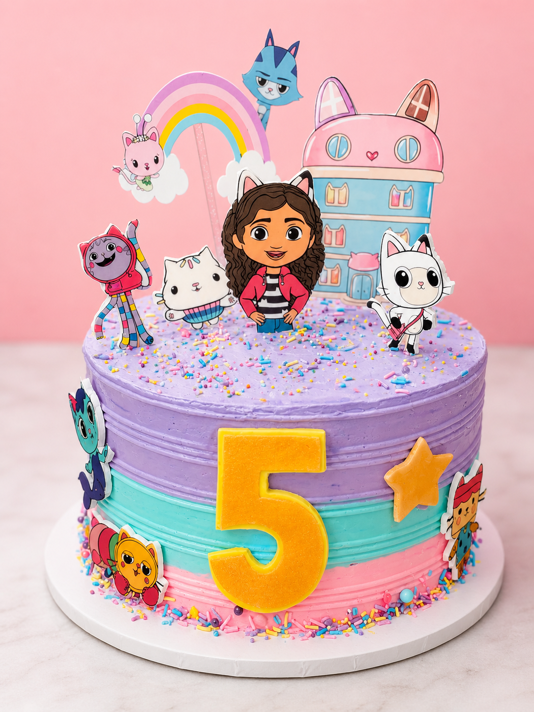 Colorful birthday cake decorated with cartoon characters, a large yellow number 5, rainbow, stars, and sprinkles on purple, pink, and blue icing.