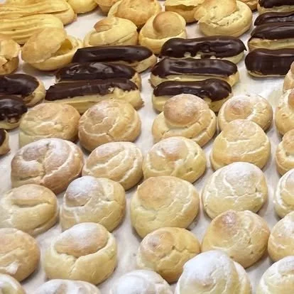 Assorted eclairs and cream puffs on a white surface.