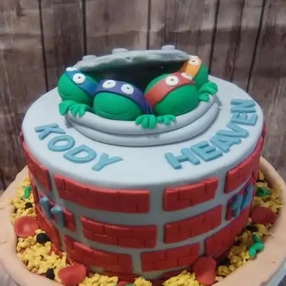 A Teenage Mutant Ninja Turtles themed cake, featuring their faces on top with the words "TOOY HEAVEN" on the side.