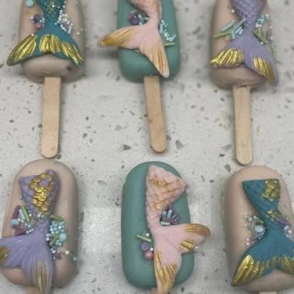 Six mermaid-themed ice cream bars with pastel-colored chocolate coating, decorated with mermaid tails, shells, and pearls.