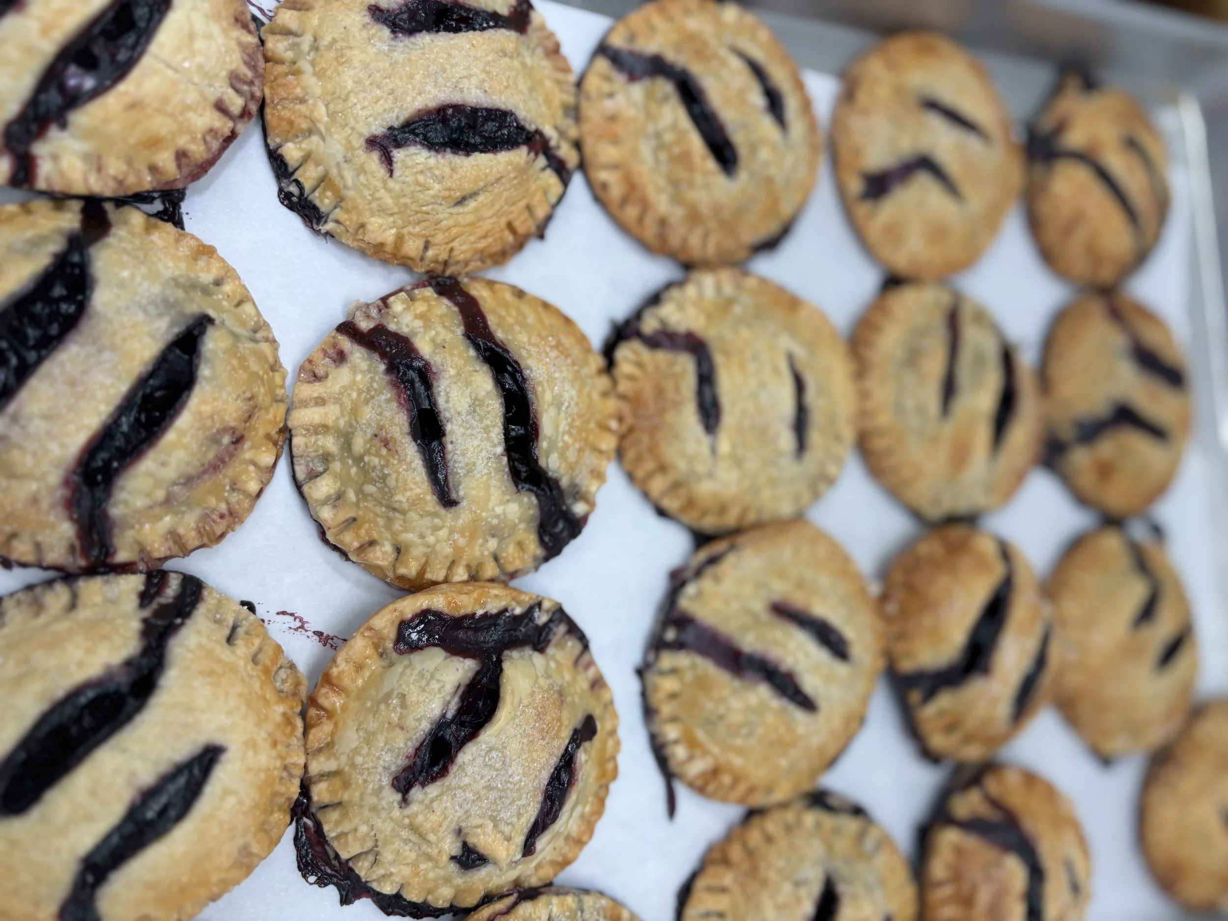Close-up of freshly baked blueberry cookies with dark purple blueberry filling on top, placed on white parchment paper.