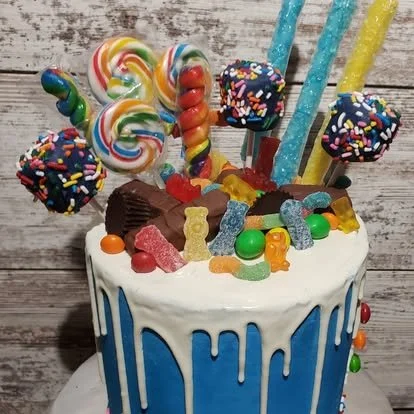 Colorful birthday cake decorated with candy, lollipops, marshmallows, gumdrops, and sprinkles, with blue and yellow candles.