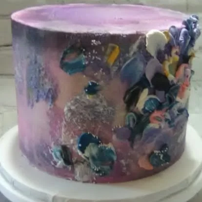 Pink and purple abstract painted cake with colorful circular patterns on the side.