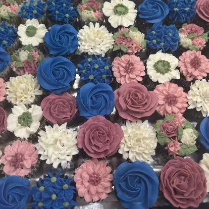 Assorted cupcakes decorated with colorful floral frosting including pink, white, blue, and purple flowers.