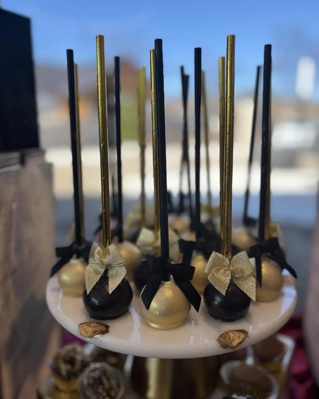 Candy apples decorated with black and gold color scheme and bows, arranged on a white plate.