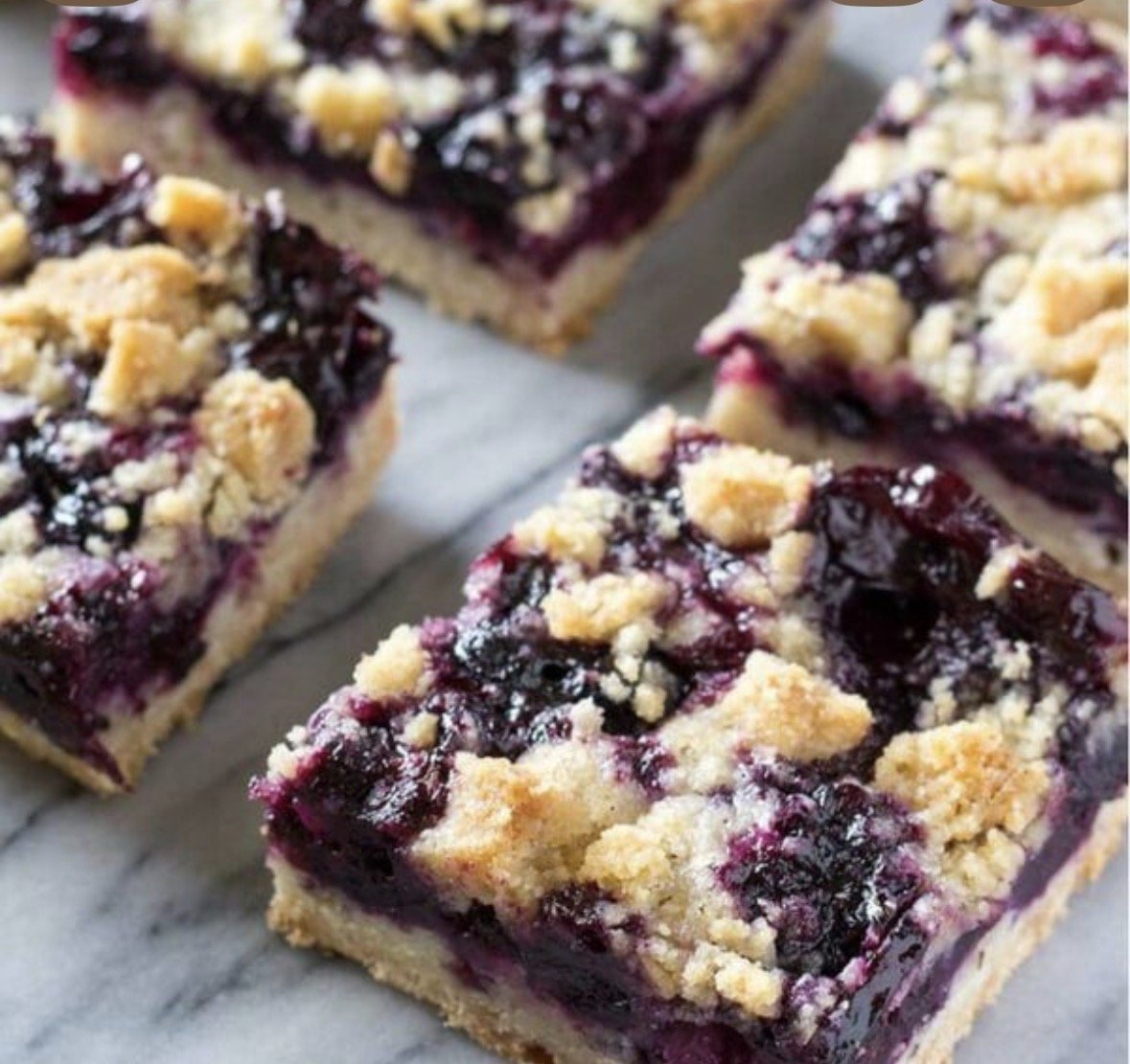 Close-up of blueberry crumble bars with a crumbly topping on a marble surface.