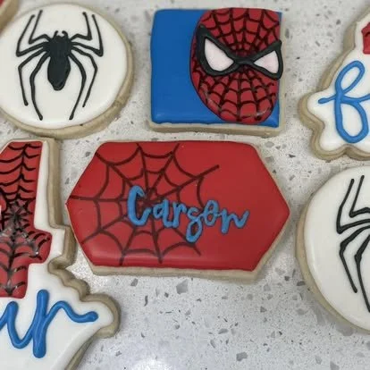 Decorated cookies with Spider-Man, Spider-Man mask, spider, and the name Carson on a red web-patterned cookie.