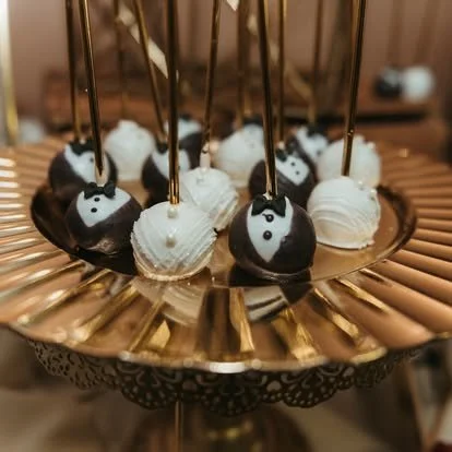 Cake pops decorated as tuxedos and bow ties on a gold tray.