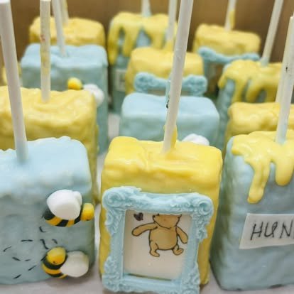 Close-up of decorated cake pops with yellow and blue icing, featuring bee and honey theme elements, including honey-looking dripping icing and a bee figurine.
