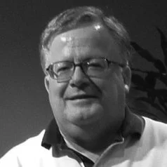 A smiling middle-aged man with glasses and short gray hair, wearing a collared shirt.
