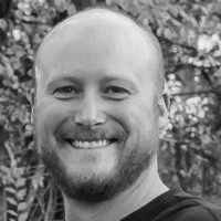 Smiling man with a beard and short hair in front of trees.