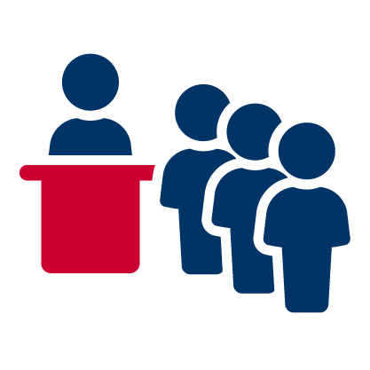 A person standing at a red podium speaking to a line of five people.