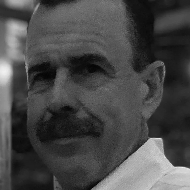 A black and white close-up portrait of a man with a mustache, looking to the side.