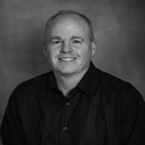 Black and white portrait of a smiling man with short hair, wearing a black shirt.
