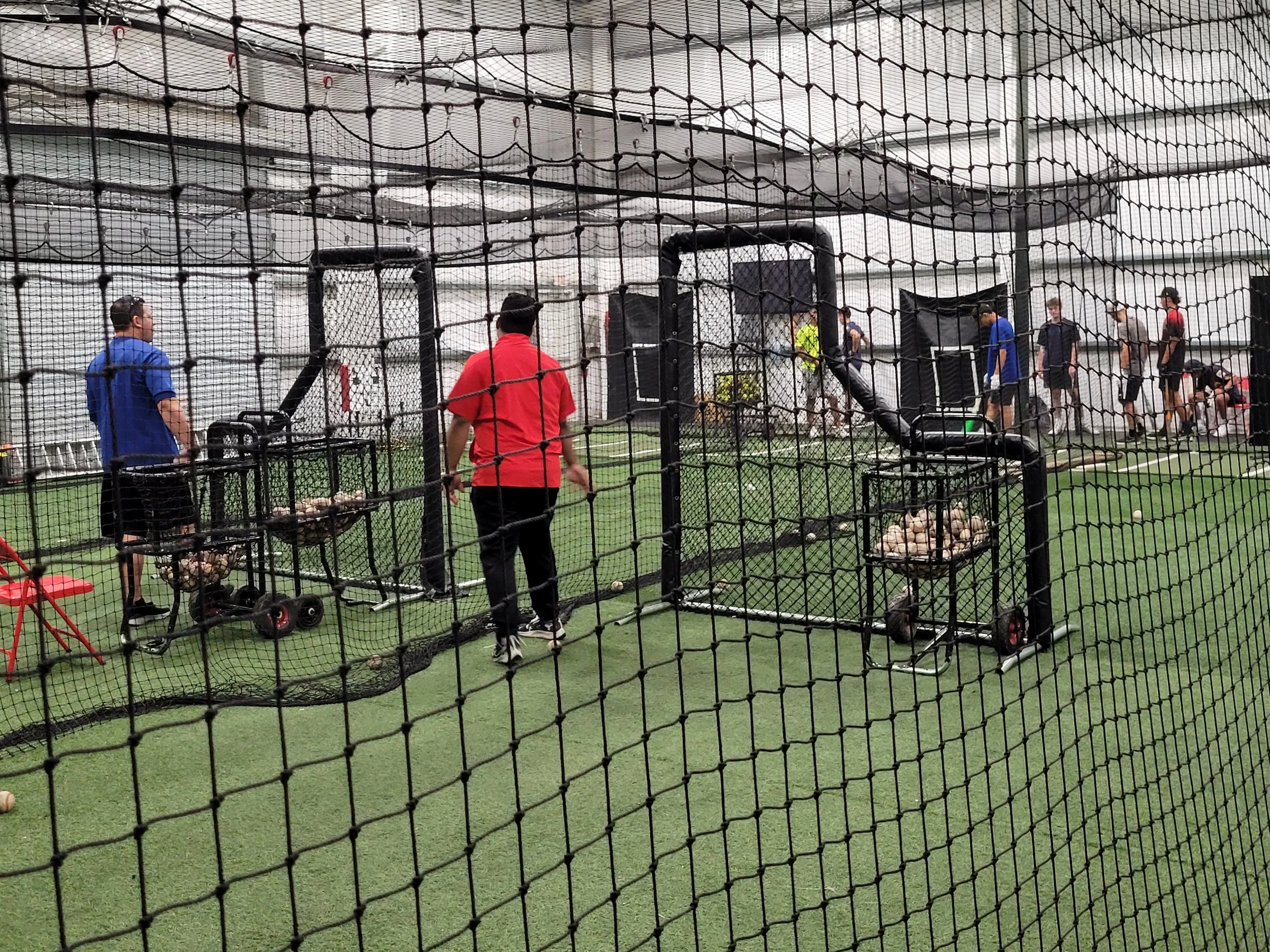 People playing baseball in an indoor batting cage, with nets surrounding the area.