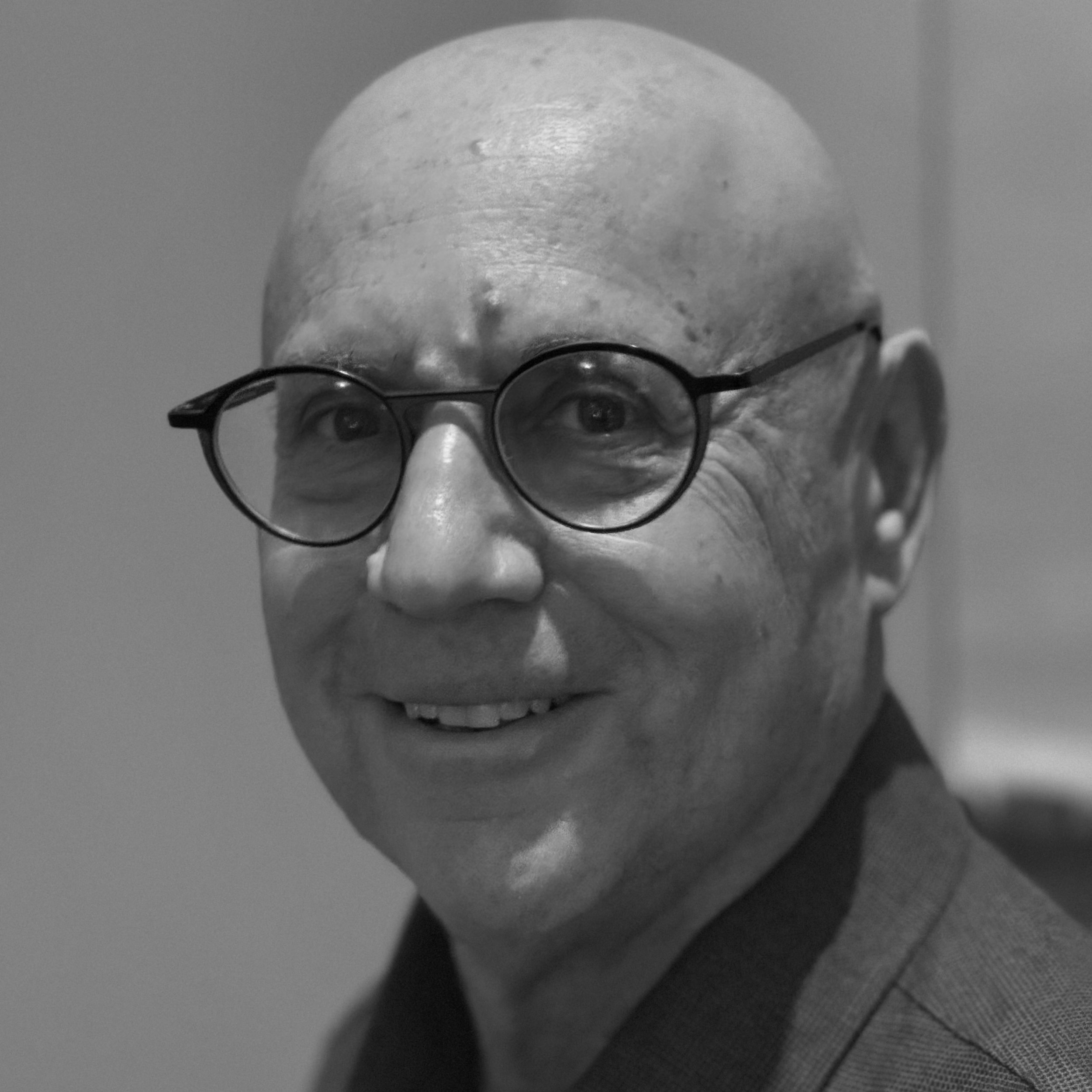 Close-up black-and-white photo of a person's head, glasses, and a serious expression, with a textured background.