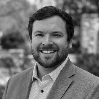 Black and white portrait of a smiling man in a suit outdoors.