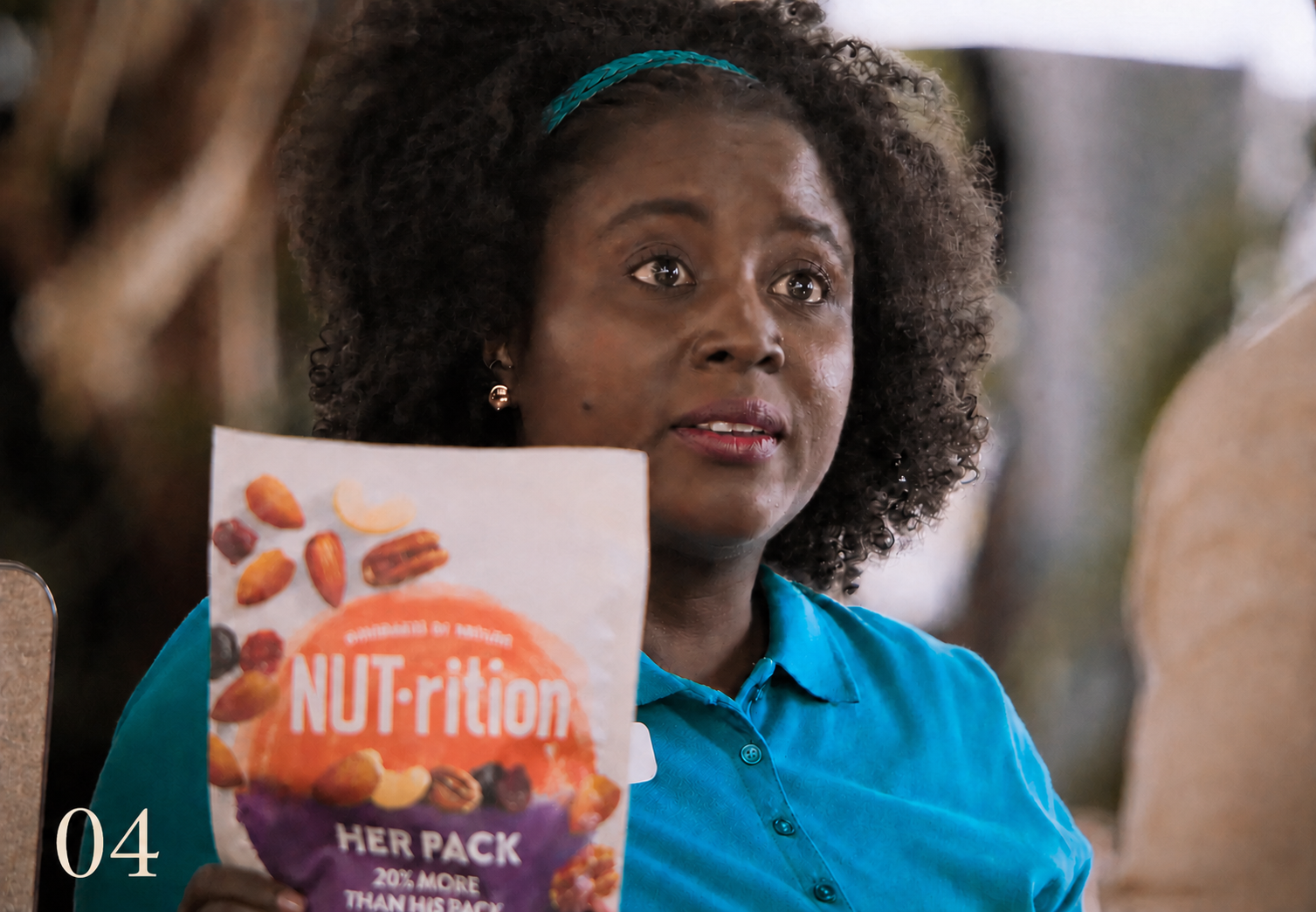 A woman in a turquoise shirt holding a NUT-rition “Her Pack” bag in the Pay Gap hidden-camera campaign.