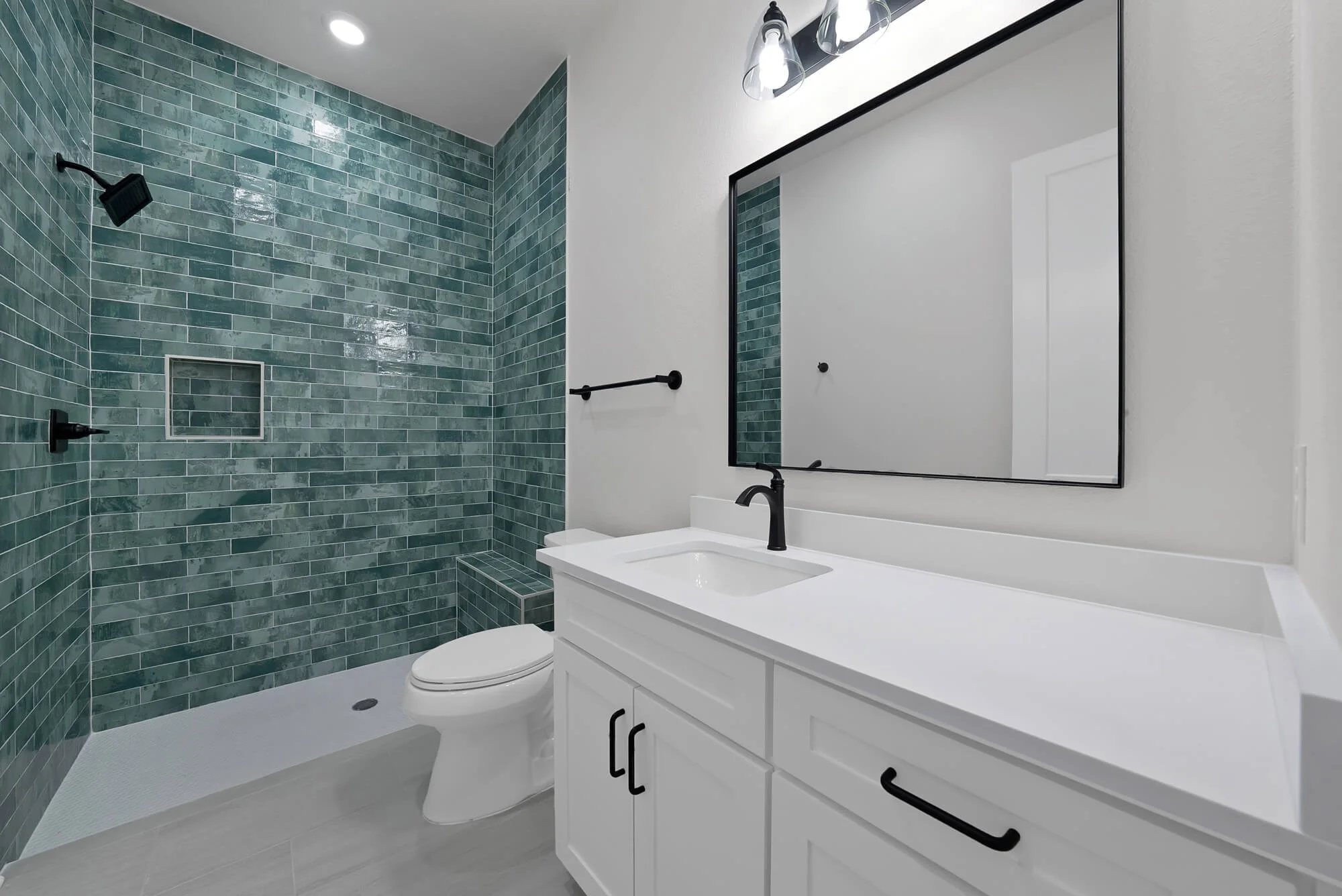 Modern bathroom featuring a walk-in shower with green subway tiles, a white vanity with black hardware, a large mirror, and black fixtures including a faucet and light fixtures.