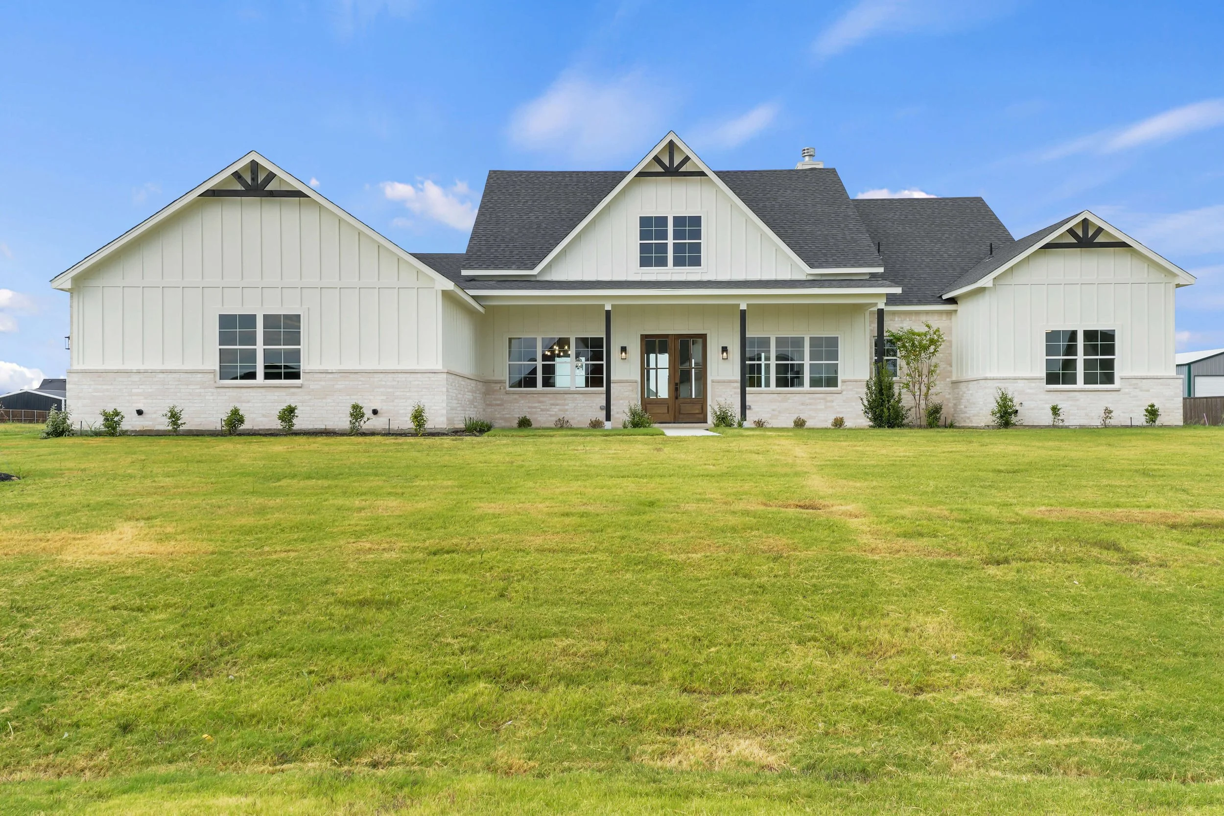A large two-story house with white siding, black trim, and a dark gray roof, situated on a well-maintained lawn, under a partly cloudy blue sky.