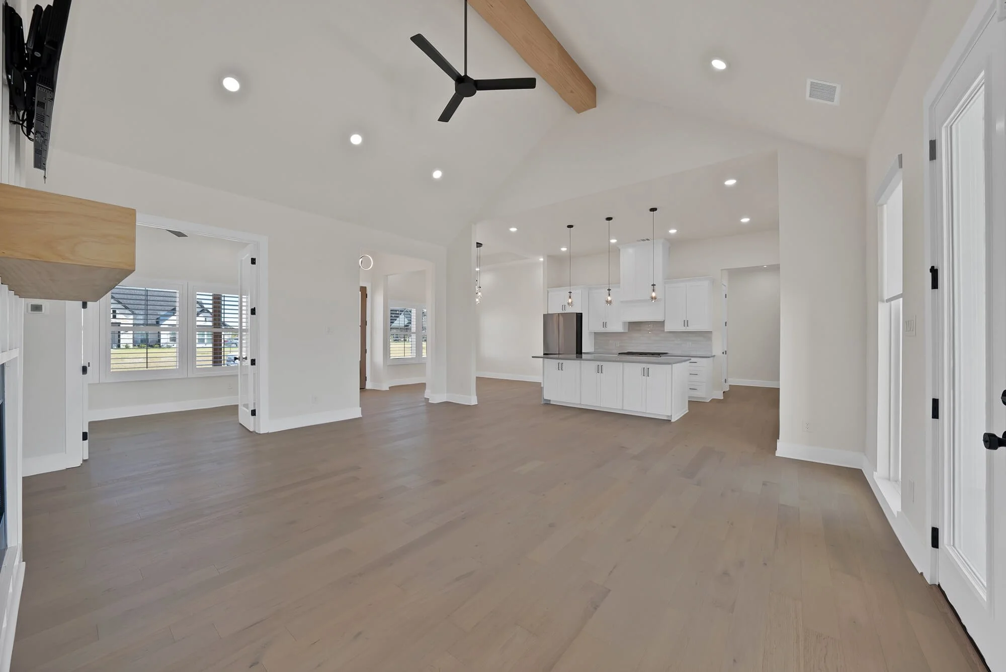 Modern open-concept kitchen and living space with white cabinets, gray backsplash, large windows, wood flooring, and a black ceiling fan.