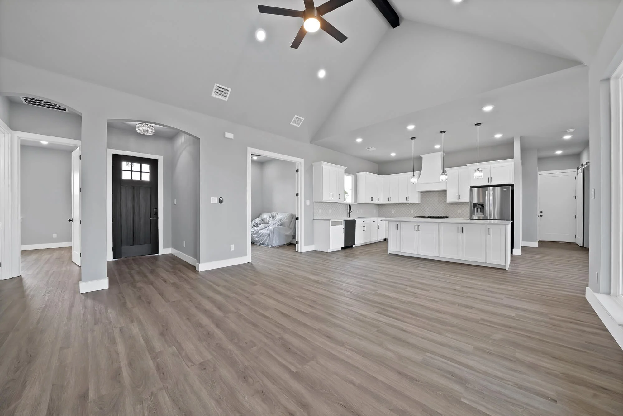 Open-concept kitchen and living area with white cabinets, stainless steel appliances, wood flooring, and vaulted ceiling with black ceiling fan.