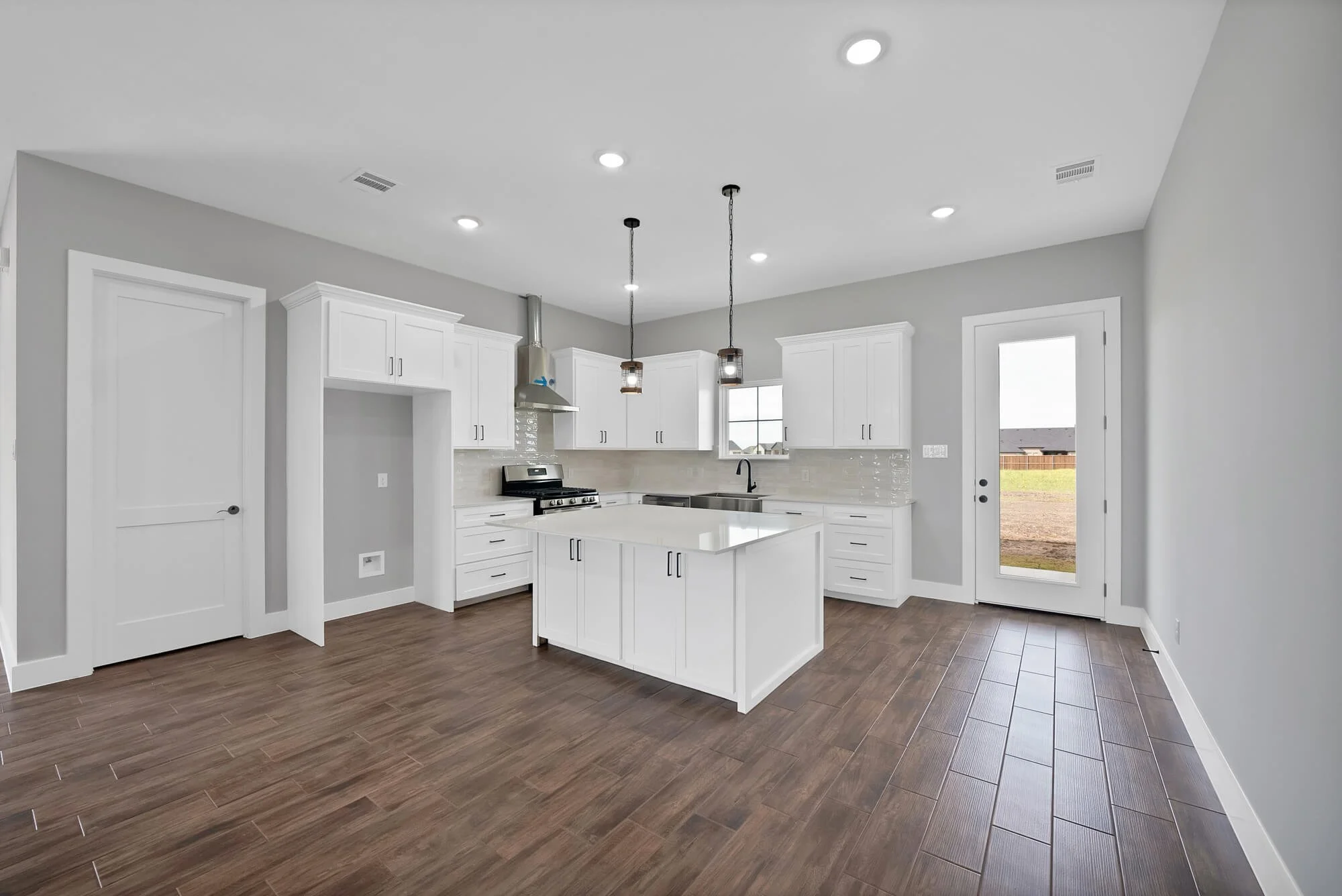 Modern kitchen with white cabinets, gray walls, dark wood flooring, stainless steel appliances, and pendant lights over a white island.