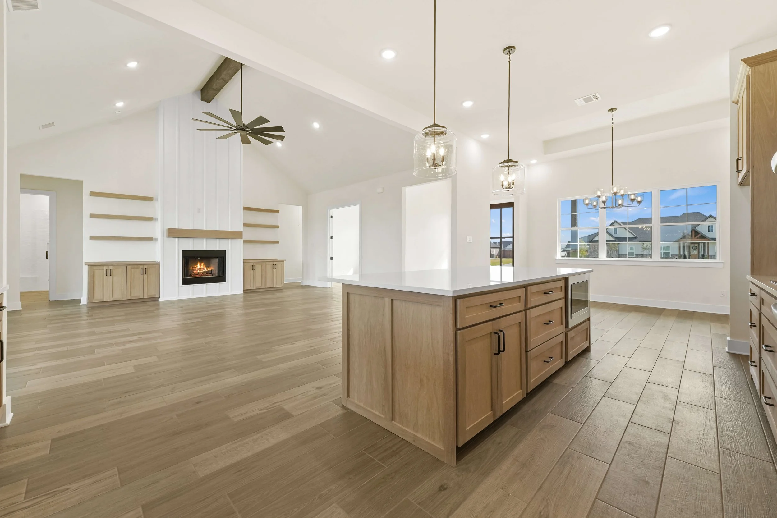 Bright open kitchen and living room with wood floors, a large window, a fireplace, and modern light fixtures.