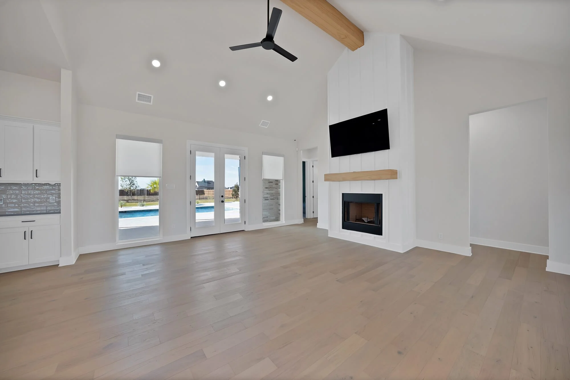 Empty living room with white walls, light wood flooring, a ceiling fan, recessed lighting, a fireplace, and large glass doors leading outside.