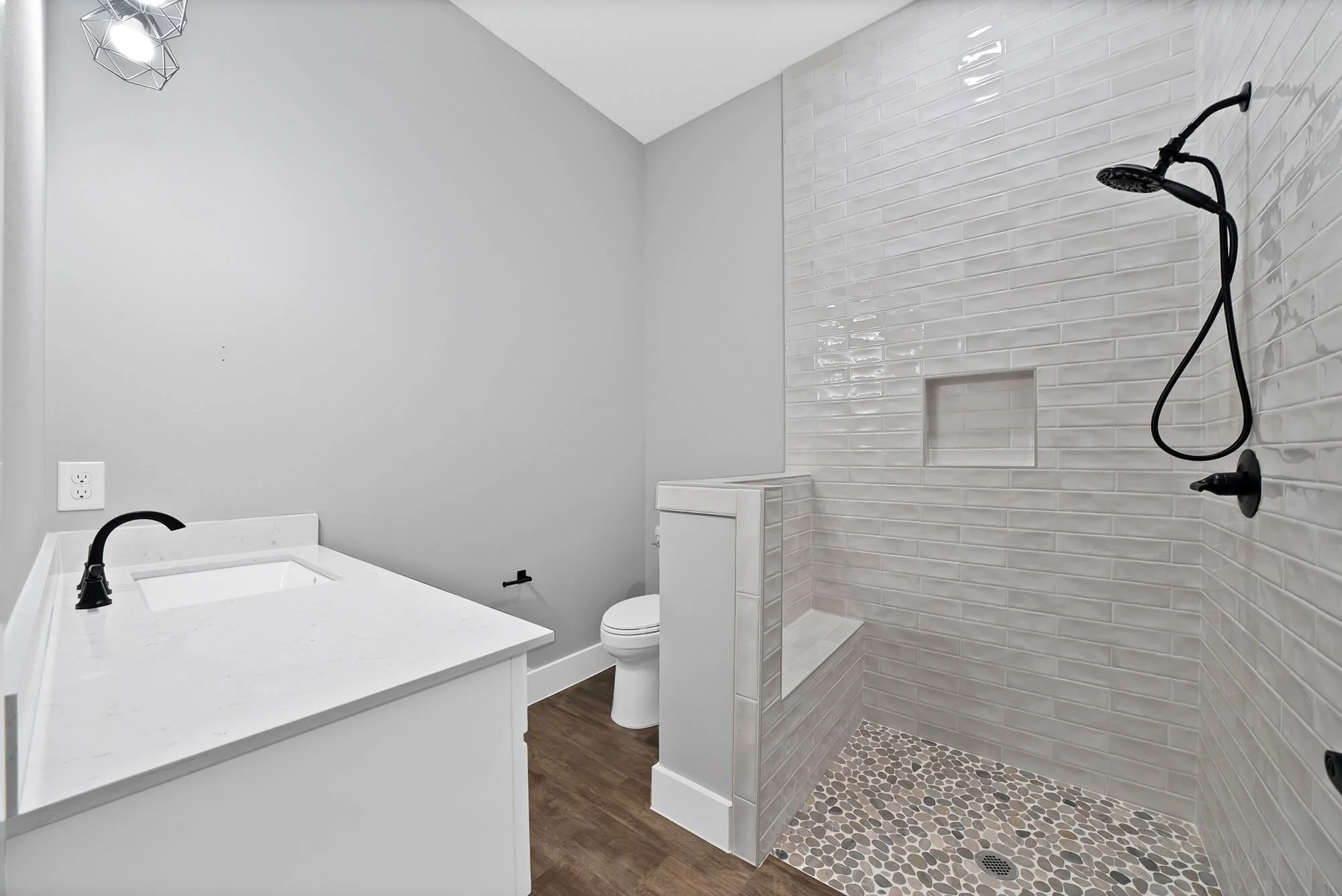 Modern bathroom with white vanity, black fixtures, toilet, and walk-in shower with white subway tiles and pebble floor.