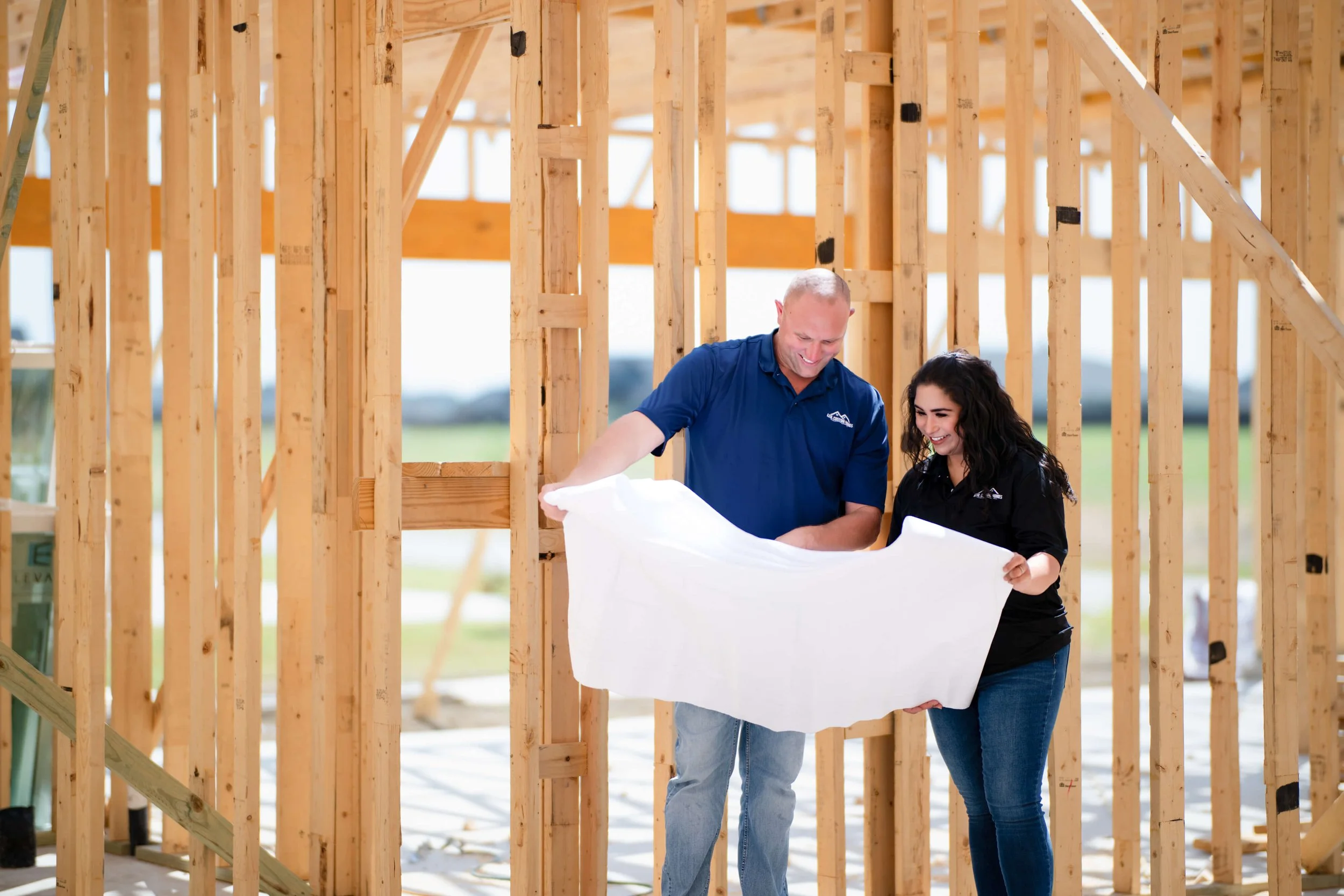 David and Tatum Abbott, owners of Azul Custom Homes,  are examining blueprints inside a wooden framed house under construction.