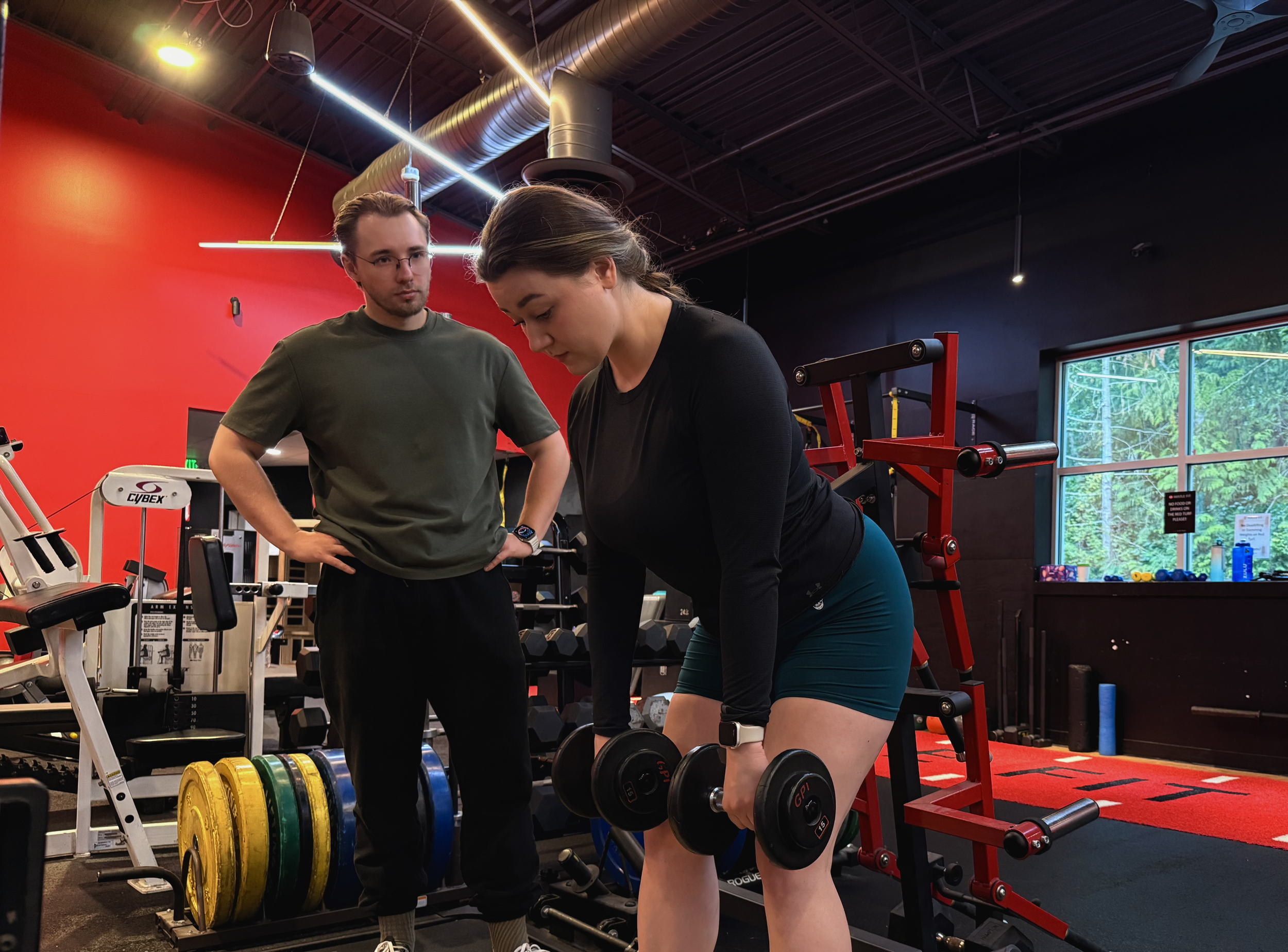 Personal trainer Bohdan Melnyk coaching a female client during a dumbbell strength training exercise at a gym in Redmond, WA.