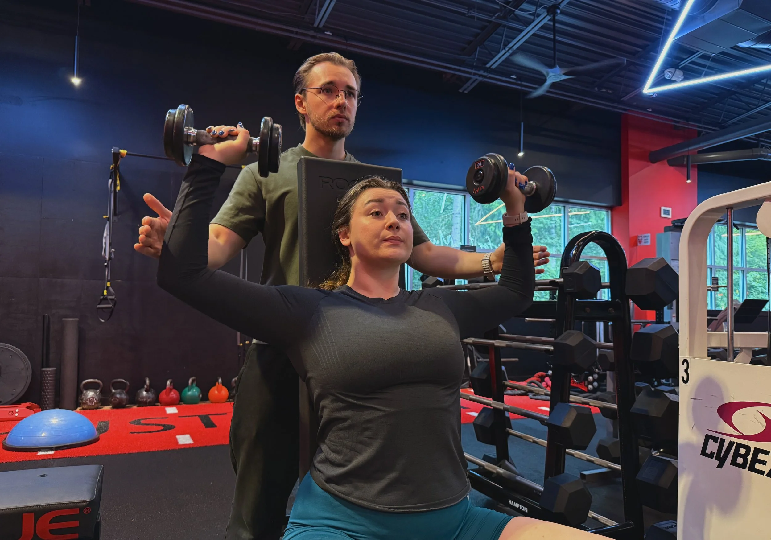 Personal trainer Bohdan Melnyk coaching a client during a shoulder press exercise at a gym in Redmond, WA.