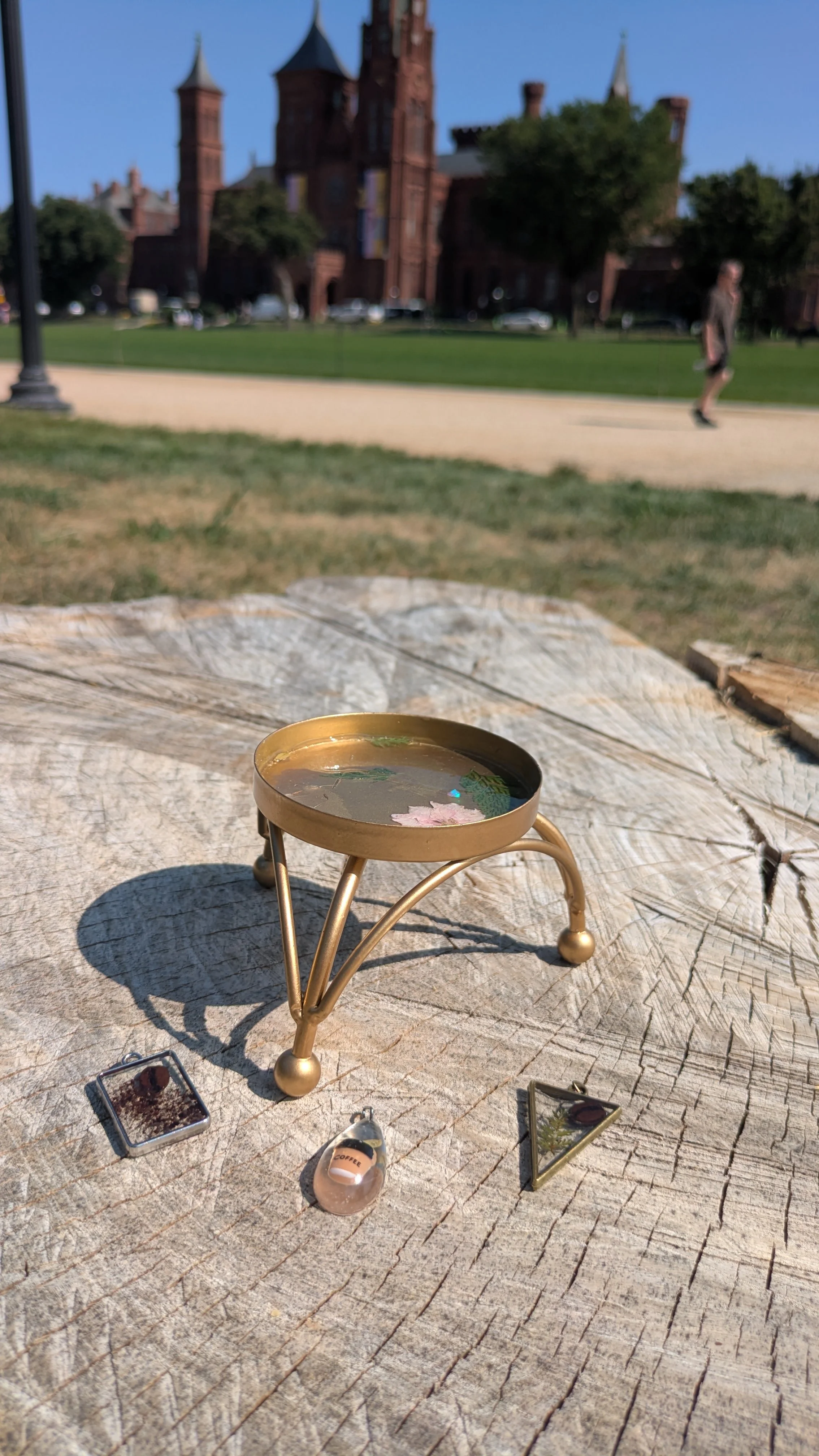 Close-up of a jewelry holder filled with resin and an opal with a flower, with small jewelry pieces with coffee inspiration, set outdoors on a sunny day.