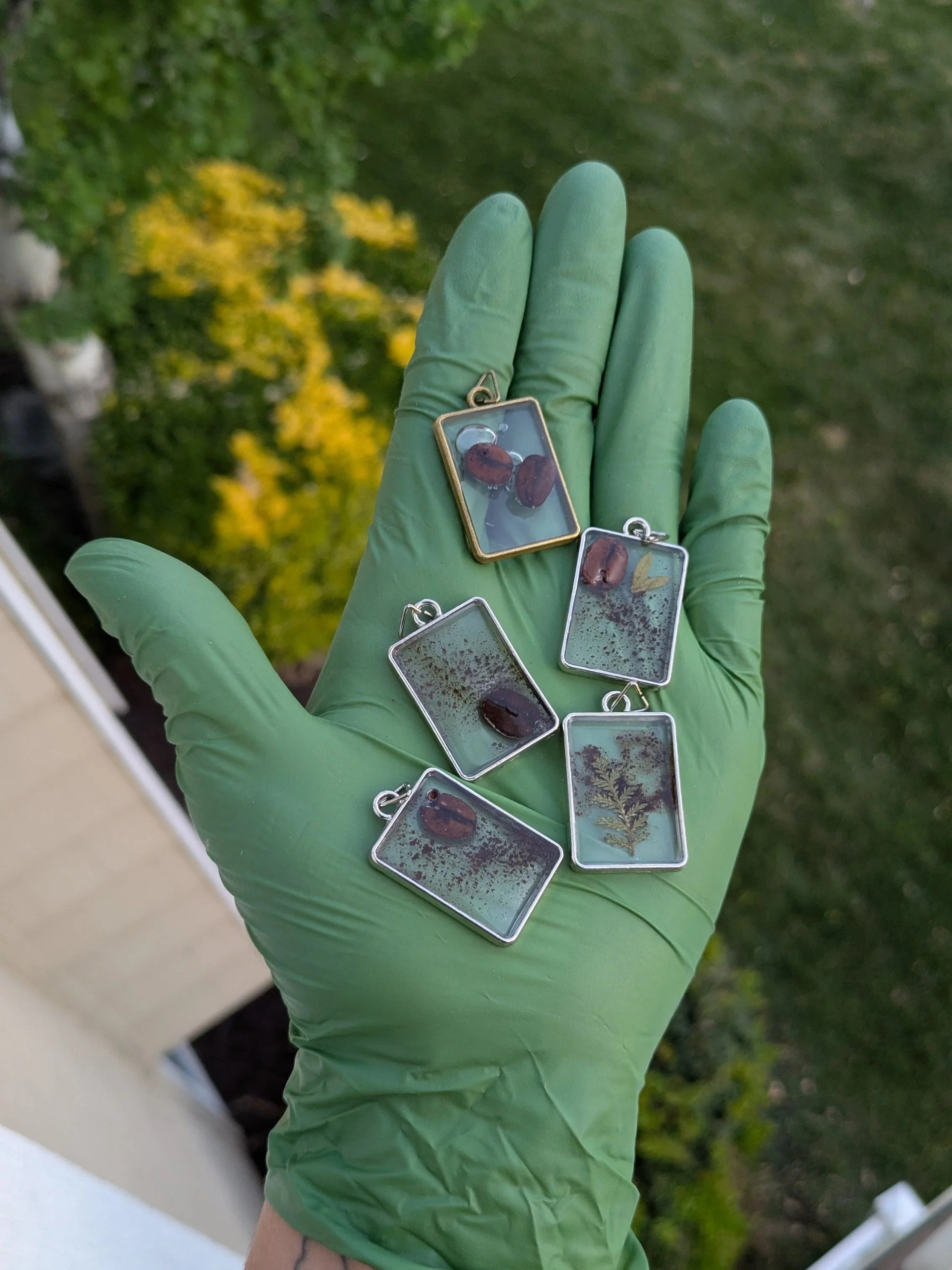 5 jewelry pieces filled with coffee beans, coffee grounds and small dainty leaves.
