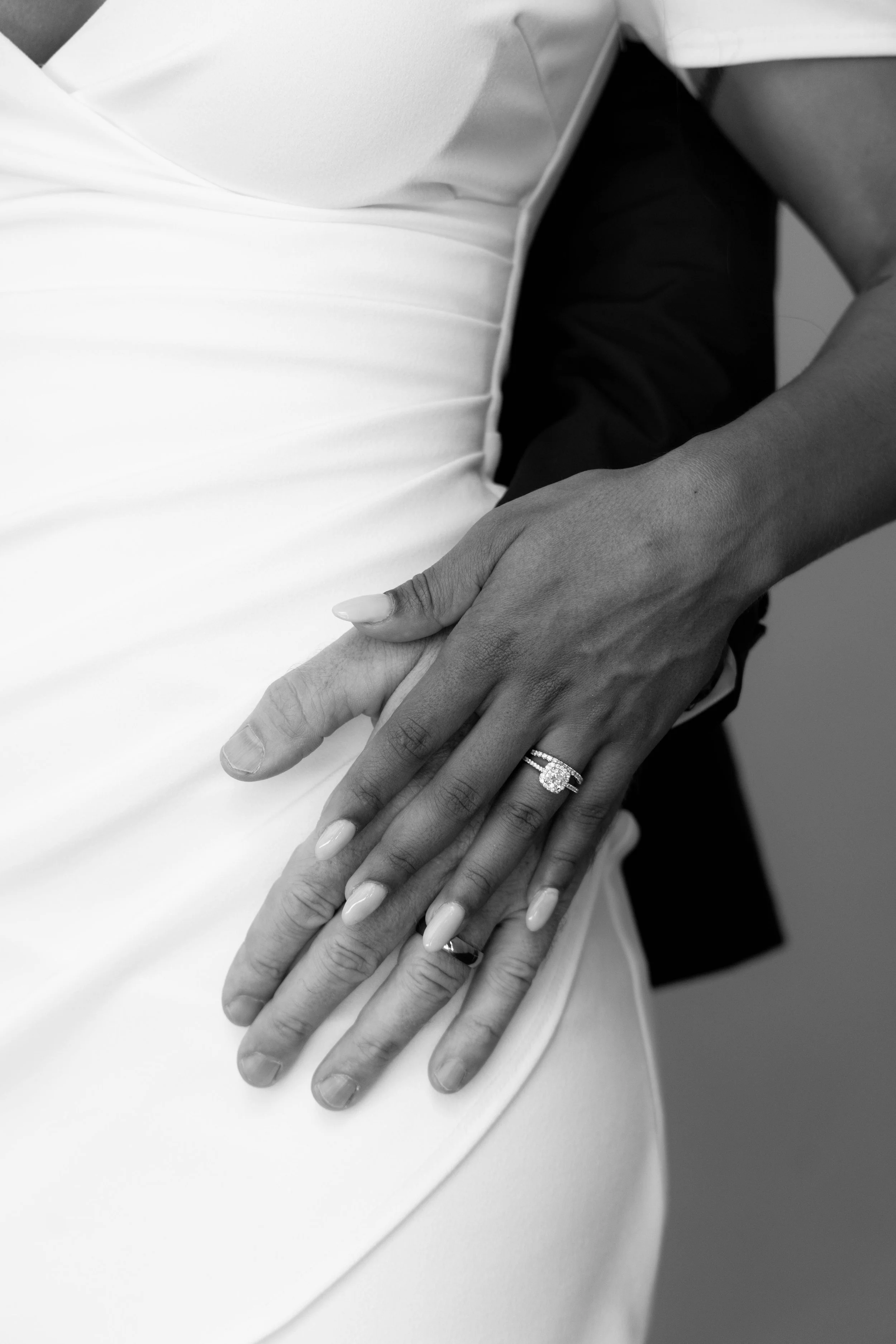 Close-up of two hands, one with an engagement ring, resting on a person's waist in a wedding dress.