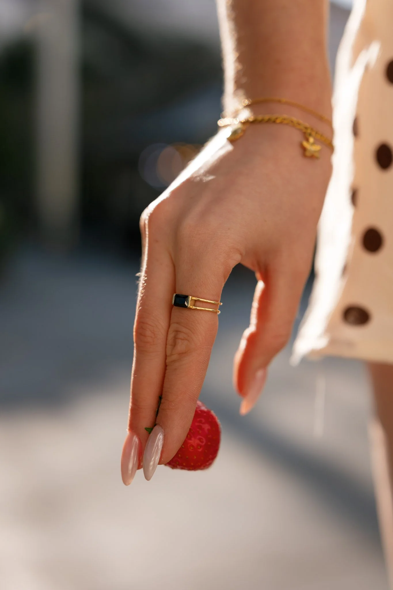 Close-up of a hand holding a strawberry, with a blurred background and a person wearing a polka-dot dress.