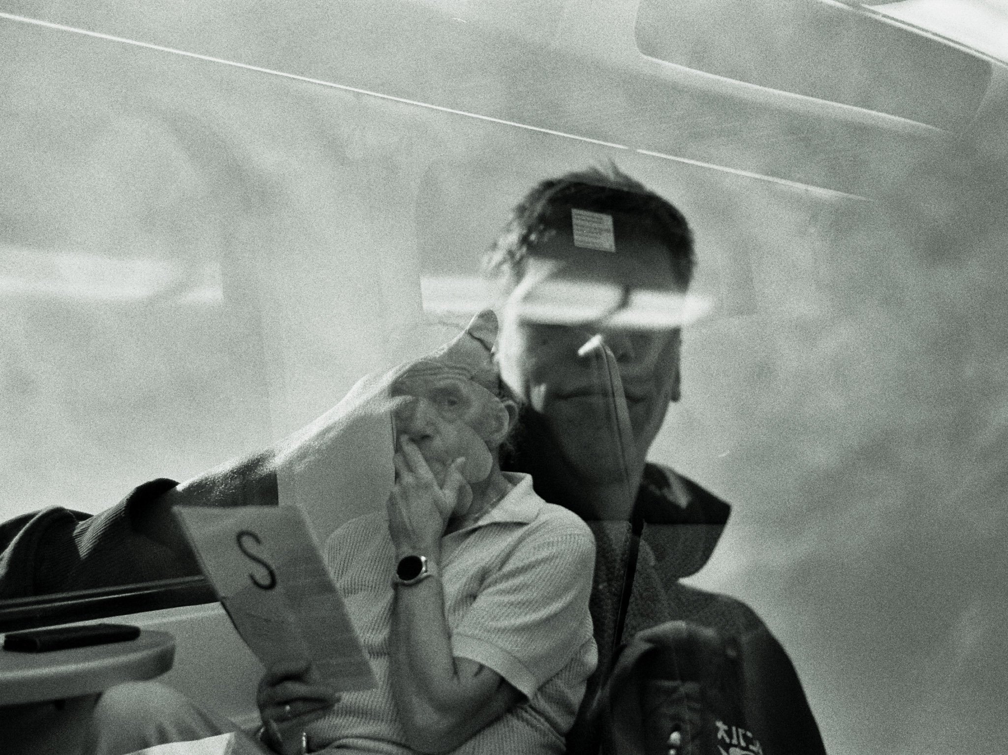 A person in a wheelchair wearing a face mask, glasses, and a jacket, sitting indoors with a reflective surface in front of them.