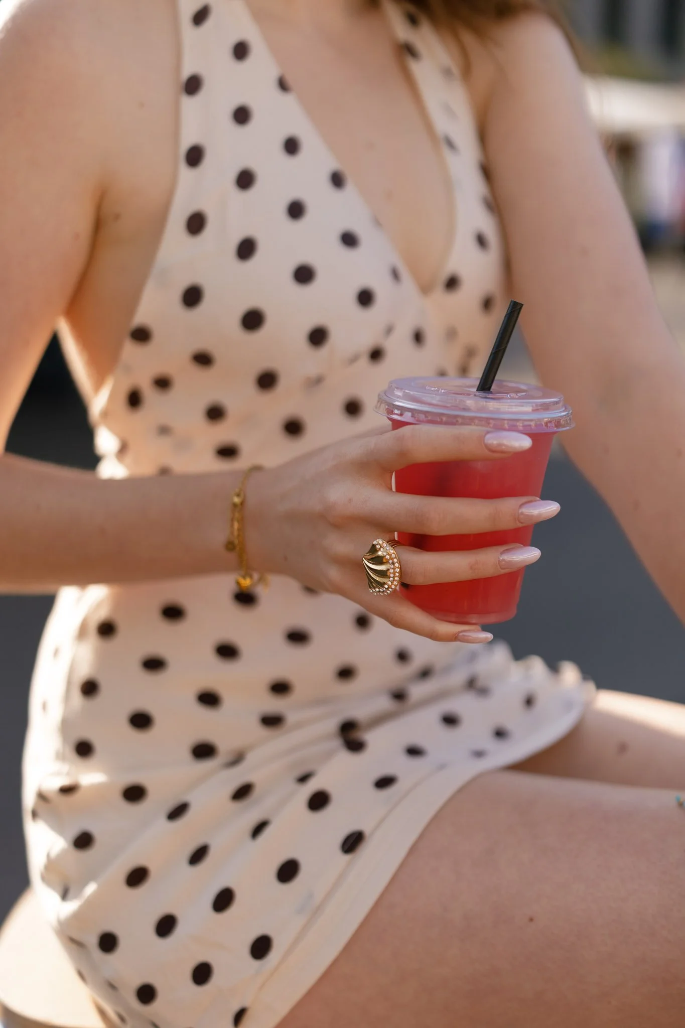 A woman in a polka dot dress holding a pink drink with a black straw.
