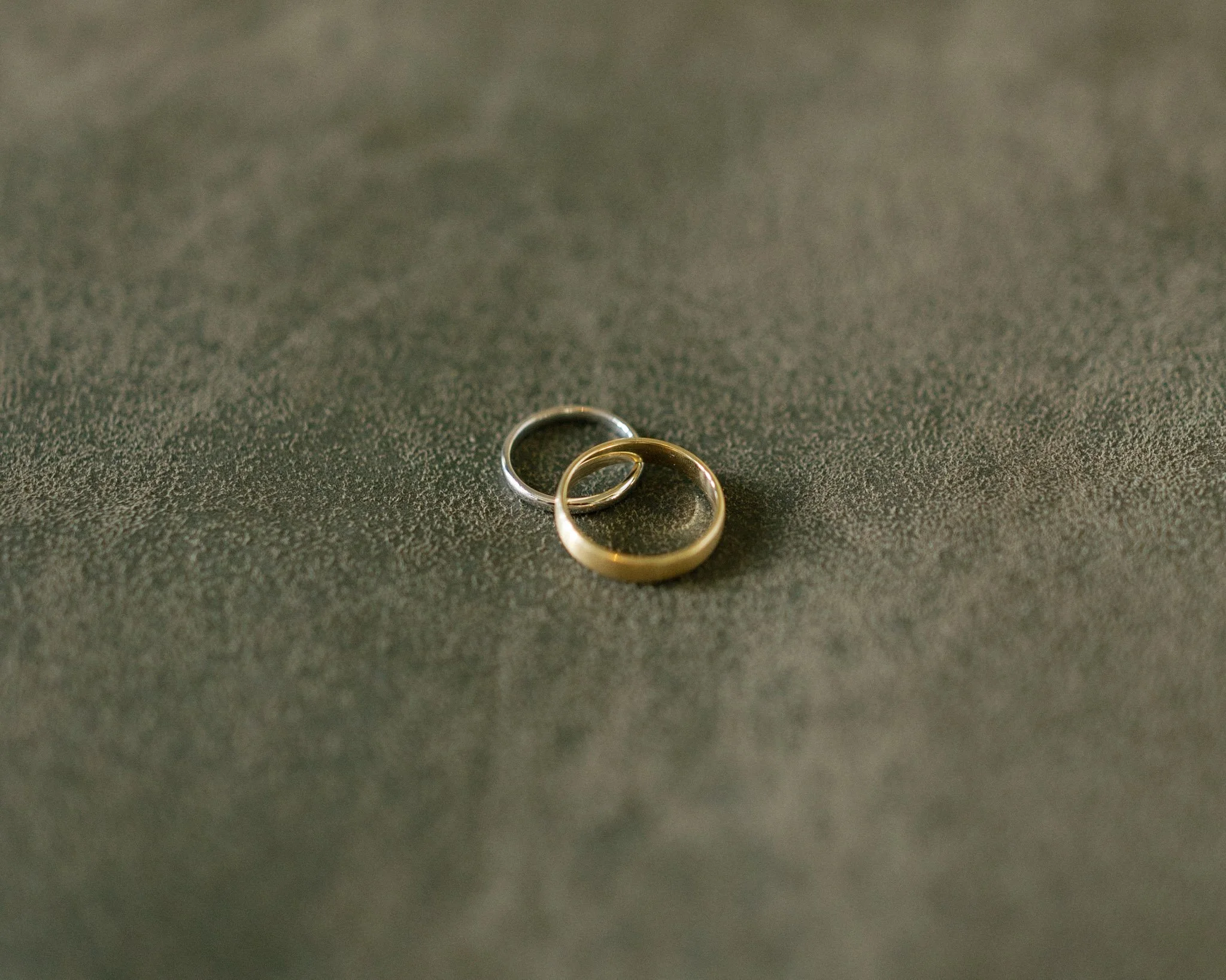 Two silver rings intertwined, lying on a dark textured surface.