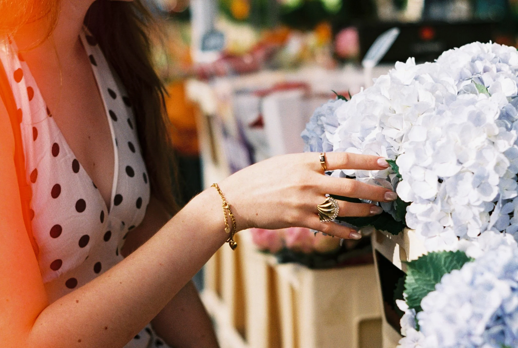 A woman wearing a polka dot shirt placing her finger on a large white hydrangea flower at a floral shop.