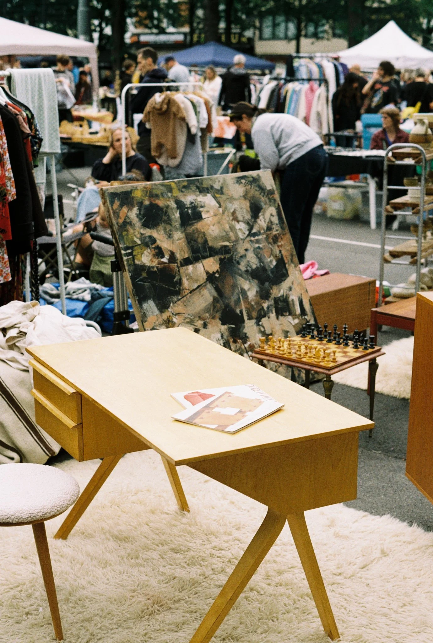 Indoor furniture and tables at a flea market or garage sale with various items displayed, including a chess set, on a cream-colored shaggy rug.
