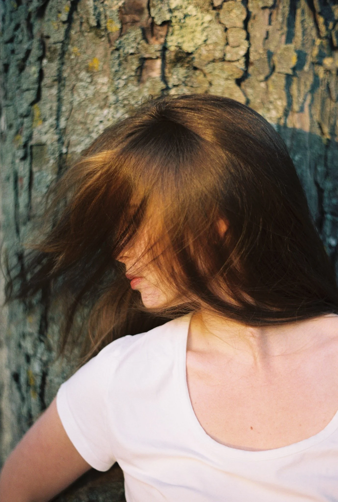 Close-up of a person's head with brown hair, wearing a white shirt, against a textured stone wall background.