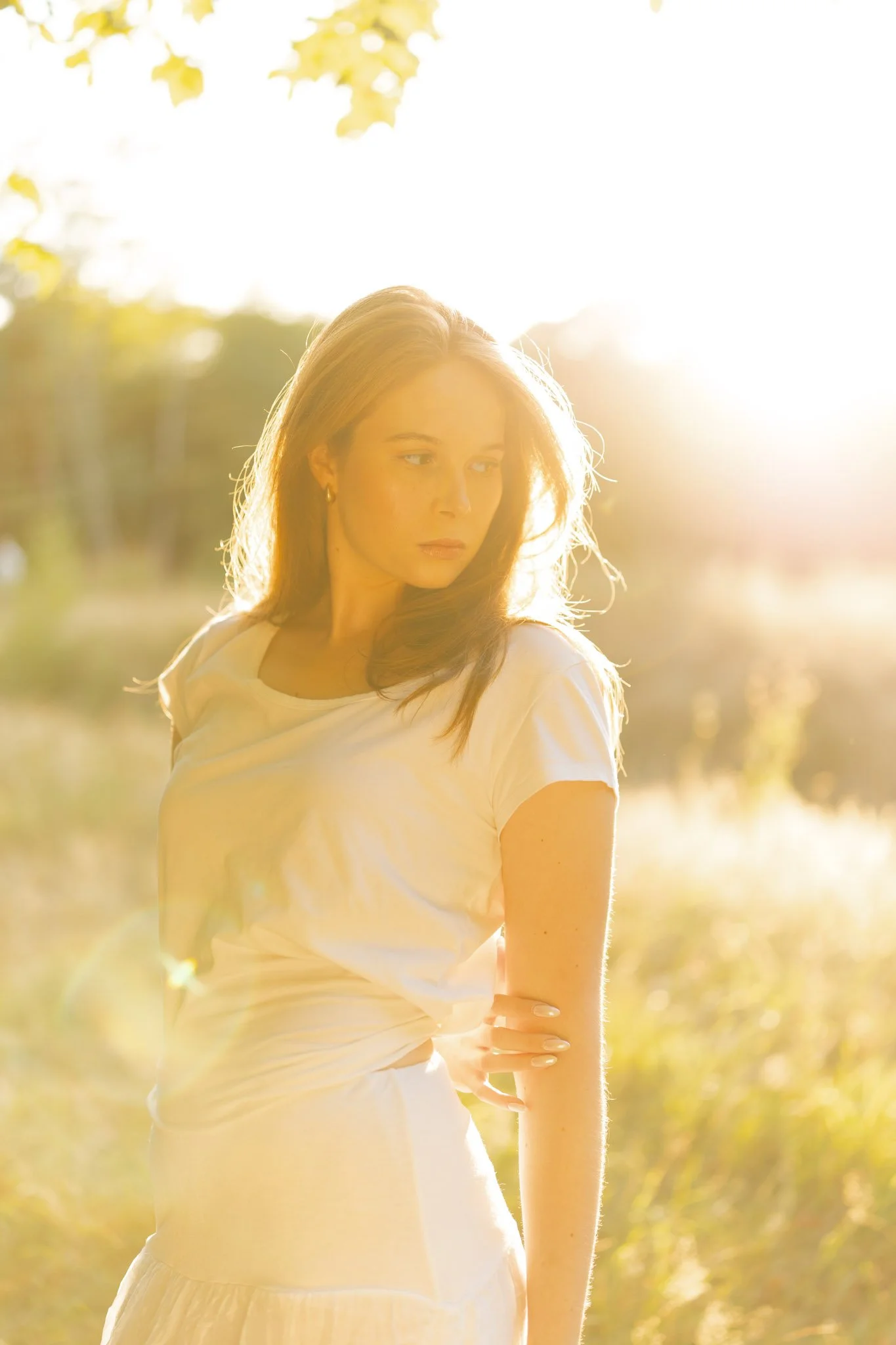 A portrait of a woman with long hair looking to the side, outdoors during sunset with sunlight creating a glow around her.